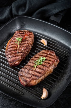 Foto de Grilled Top Blade or flat iron roast beef meat steaks on a skillet. Black background. Top View. - Imagen libre de derechos