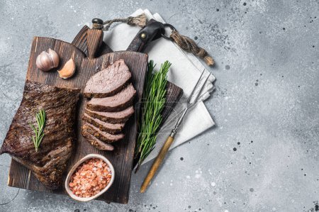 Téléchargez les photos : Roast and sliced tri tip beef steak on a wooden board with herbs. Gray background. Top view. Copy space. - en image libre de droit