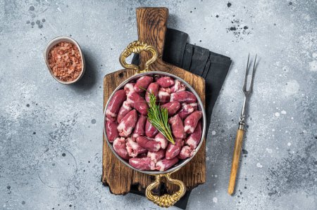 Fresh raw chicken hearts in a skillet with herbs. Gray background. Top view.