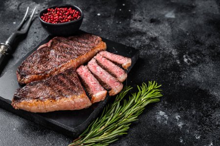 Téléchargez les photos : Surlonge grillée ou steak de viande de bœuf croustillant sur du marbre. Fond noir. Vue de dessus. Espace de copie. - en image libre de droit