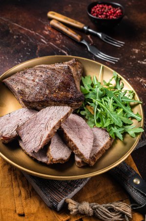 Téléchargez les photos : Rôti Tri Tip ou surlonge steak de bœuf sur une assiette avec roquette. Fond sombre. Vue du dessus. - en image libre de droit