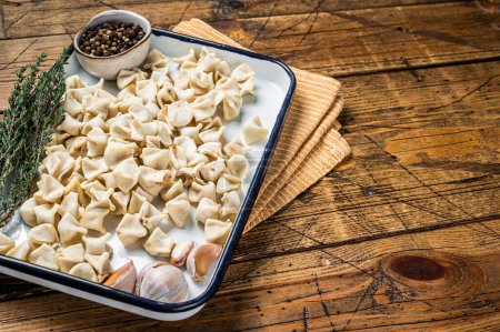 Foto de Raw Manti Dumpling with meat in tray with herbs and spices. Wooden background. Top view. Copy space. - Imagen libre de derechos