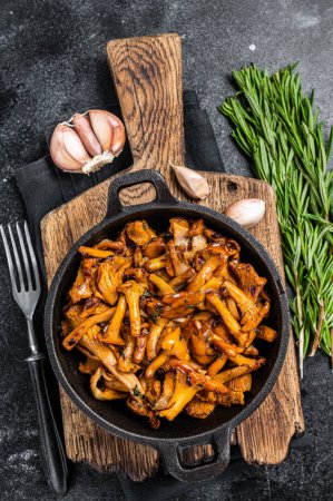 Photo for French roasted chanterelle mushrooms with onions and thyme in a pan. Black background. Top view. - Royalty Free Image