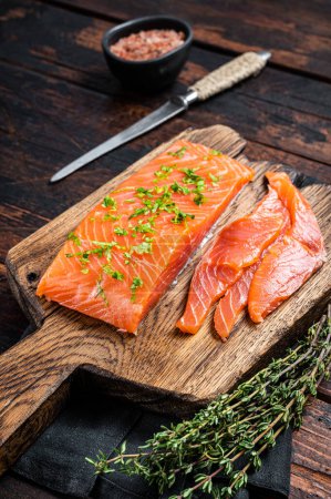 Sliced Salted salmon fillet with herbs on a wooden board. Wooden background. Top view.