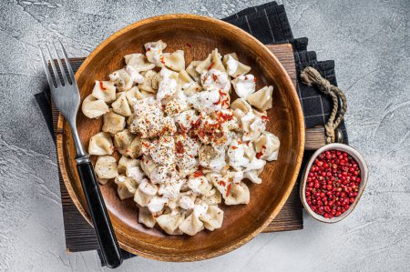 Foto de Manti Dumpling with yoghurt and tomato sauce in a wooden plate. White background. Top view. - Imagen libre de derechos