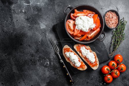 Crusty Bruschettas toasts with stracciatella cheese, chopped tomatoes and thyme. Black background. Top view. Copy space.