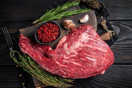 Tri Tip black angus beef steak on cutting board with herbs, raw meat. Black Wooden background. Top view.