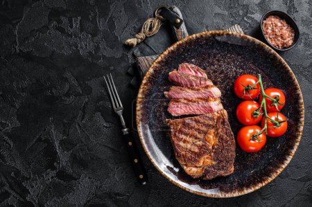 Téléchargez les photos : Bifteck aux côtes grillées, viande marbrée de bœuf côtelé dans une assiette avec tomate. Fond noir. vue de dessus. Espace de copie. - en image libre de droit