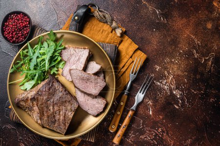 Téléchargez les photos : Roast Tri Tip or sirloin bottom beef steak on a plate with arugula. Dark background. Top view. Copy space. - en image libre de droit