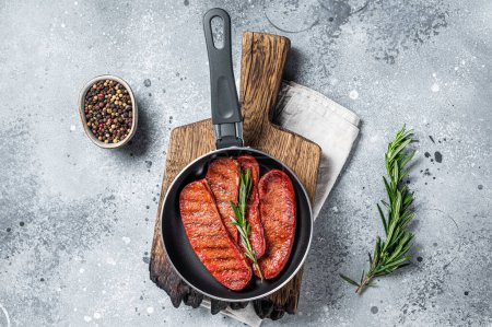 Cooking of Turkish Sucuk beef meat sausage in a skillet. Gray background. Top view.