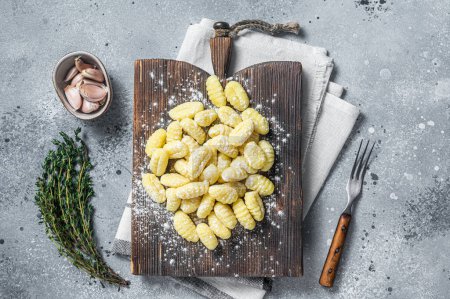 Photo for Raw homemade potato gnocchi with fork on wooden cutting board. Gray background. Top view. - Royalty Free Image