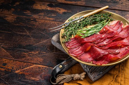 Photo for Basturma, sliced dried beef meat, meat Jerky in steel plate with herbs and spices. Wooden background. Top view. Copy space. - Royalty Free Image