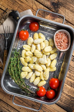 Photo for Uncooked Raw potato gnocchi in kitchen steel tray with herbs. Wooden background. Top view. - Royalty Free Image