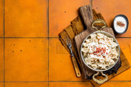 Foto de Turkish traditional manti with yoghurt and tomato sauce in a skillet. Orange background. Top view. Copy space. - Imagen libre de derechos