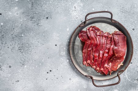 Photo for Sliced basturma, cured beef meat in steel tray. Gray background. Top view. Copy space. - Royalty Free Image
