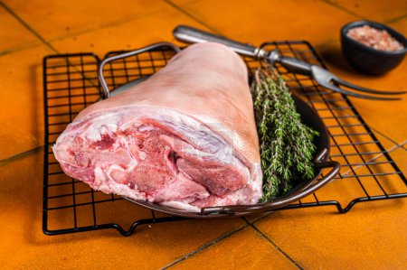 Photo for Raw pork shank knuckle in a steel tray with herbs. Orange background. Top view. - Royalty Free Image