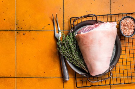 Photo for Raw pork shank knuckle in a steel tray with herbs. Orange background. Top view. Copy space. - Royalty Free Image