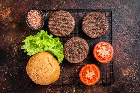 Téléchargez les photos : Grilled hamburger patties with tomatoes and seasonings on kitchen table. Dark background. Top view. - en image libre de droit