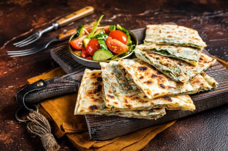 Freshly baked Turkish Gozleme, flatbread with greens and cheese. Dark background. Top view.