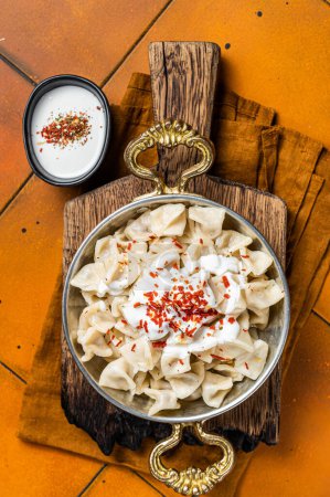 Foto de Turkish traditional manti with yoghurt and tomato sauce in a skillet. Orange background. Top view. - Imagen libre de derechos