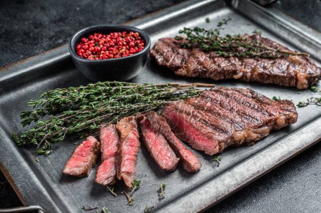 BBQ roast denver top blade beef meat steak on a steel tray with herbs. Black background. Top view.