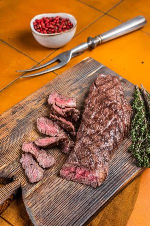 Grilled Medium Rare Machete or skirt beef meat steak on wooden cutting board. Orange background. Top view.