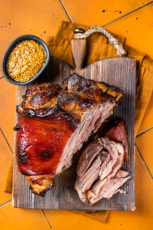 Photo for Roasted pork Shank, knuckle on a wooden board. Orange background. Top view. - Royalty Free Image