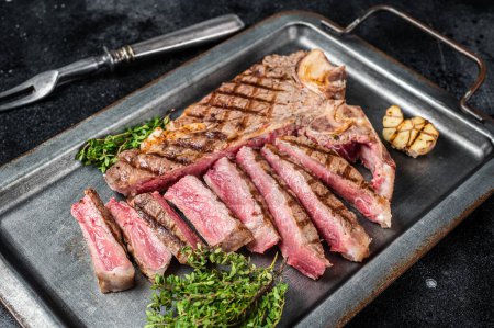 Medium rare Grilled T-Bone Steak, Florentine steak sliced in a steel tray. Black background. Top view.