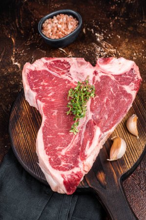 Raw Porterhouse steak, marbled beef meat on a wooden board. Dark background. Top view.
