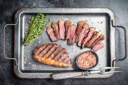 Fried and sliced Top sirloin steak, Grilled cup rump beef meat steak on a steel serving tray with spices. Black background. Top view.