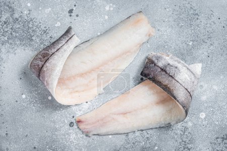 Téléchargez les photos : Two raw haddock fish fillets on kitchen table. Gray background. Top view. - en image libre de droit