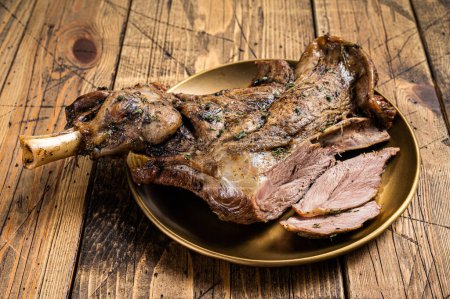 Baked whole lamb shoulder leg with herbs and spices in a steel plate. Wooden background. Top view.