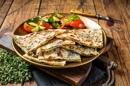 Gozleme flatbread with greens and vegetable salad on garnish. Wooden background. Top view.