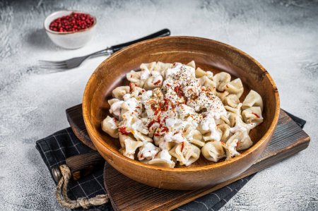 Manti Dumpling with yoghurt and tomato sauce in a wooden plate. White background. Top view.