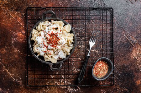 Foto de Cooking Manti Dumpling with yoghurt and tomato sauce in a skillet. Dark background. Top view. - Imagen libre de derechos
