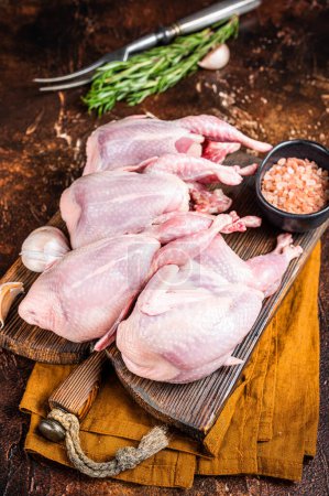 Plucked raw quails, fresh poultry on wooden board with spices. Dark background. Top view.