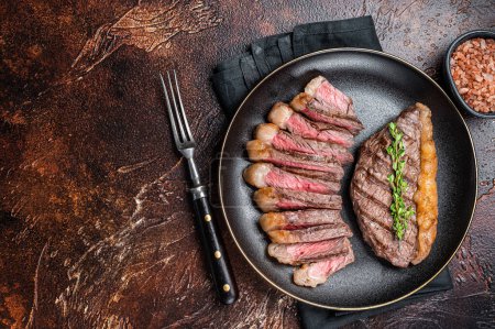 Téléchargez les photos : Tranché grillé moyen rare Haut surlonge steak de bœuf sur une assiette. Fond sombre. Vue de dessus. Espace de copie. - en image libre de droit