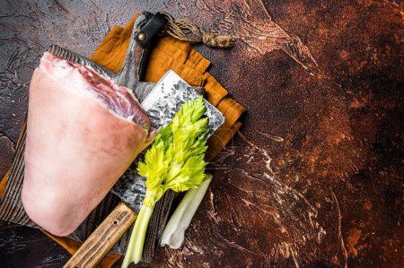 Fresh Raw pork shank knuckle on a butcher board with herbs for cooking. Dark background. Top view. Copy space.