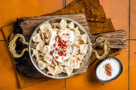 Foto de Turkish traditional manti with yoghurt and tomato sauce in a skillet. Orange background. Top view. - Imagen libre de derechos