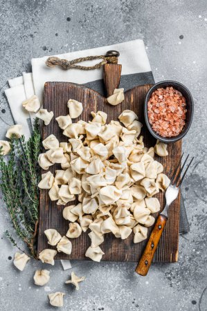 Foto de Uncooked Manti Dumpling on wooden board with herbs, raw food. Gray background. Top view. - Imagen libre de derechos
