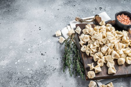 Foto de Uncooked Manti Dumpling on wooden board with herbs, raw food. Gray background. Top view. Copy space. - Imagen libre de derechos