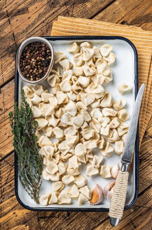 Raw Manti Dumpling with meat in tray with herbs and spices. Wooden background. Top view.