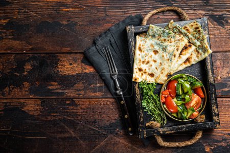 Baked Gozleme flatbread with greens in a box with vegetable salad. Wooden background. Top view. Copy space.