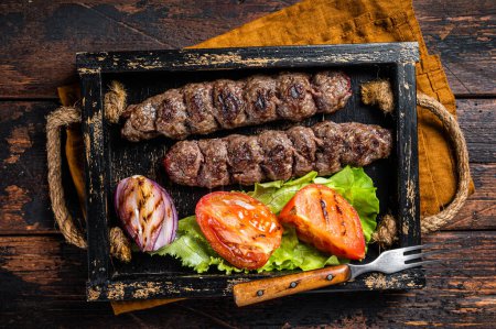 Traditional middle east kefta or kofta kebab, ground beef and lamb meat grilled on skewers served with tomato, salad and onion. Wooden background. Top view.