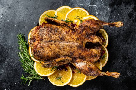 Christmas dinner, baked duck with rosemary and oranges, crispy whole roast duck. Black background. Top view.