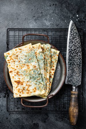 Gozleme Turkish flatbread with greens and cheese. Black background. Top view.