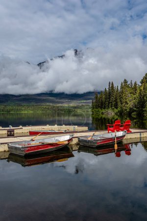 Téléchargez les photos : Low clouds on a still morning at the Pyramid Lake, Jasper National Park dock with boats and red chairs - en image libre de droit