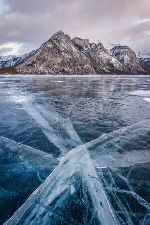 Téléchargez les photos : Fissures dans la glace du lac Minnewanka avec le mont Inglismaldie dans le parc national Banff en arrière-plan - en image libre de droit
