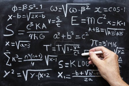 Hand writing mathematical operations and quantum physics formulas with a chalk on the blackboard