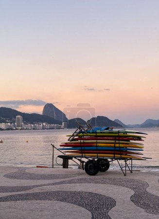Téléchargez les photos : Rio de Janeiro, Brésil, 07-06-2023 : planches de surf empilées sur un chariot au coucher du soleil sur la plage d'Ipanema, l'une des plages les plus célèbres au monde, avec le trottoir graphique emblématique le long de l'Avenida Atlantica - en image libre de droit
